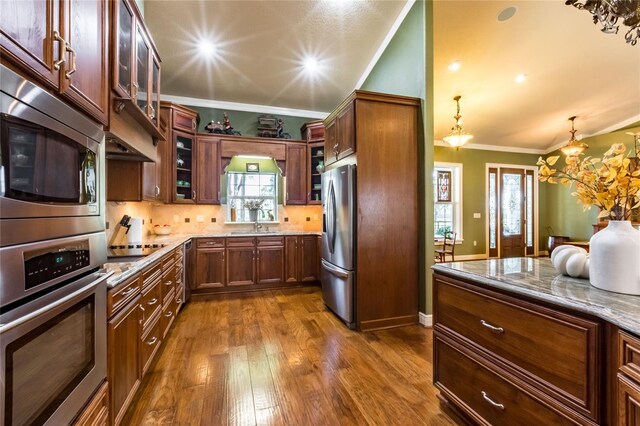 kitchen featuring ornamental molding, dark hardwood / wood-style flooring, decorative backsplash, light stone countertops, and stainless steel appliances