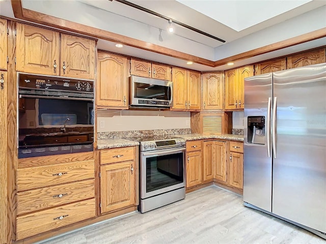 kitchen with rail lighting, light wood-type flooring, light stone counters, and stainless steel appliances