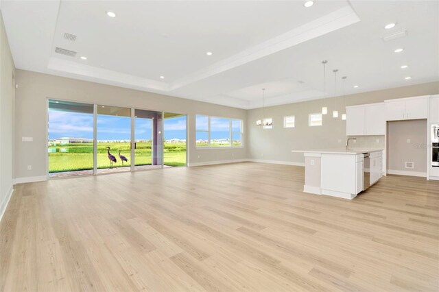 unfurnished living room with sink, light hardwood / wood-style flooring, and a tray ceiling