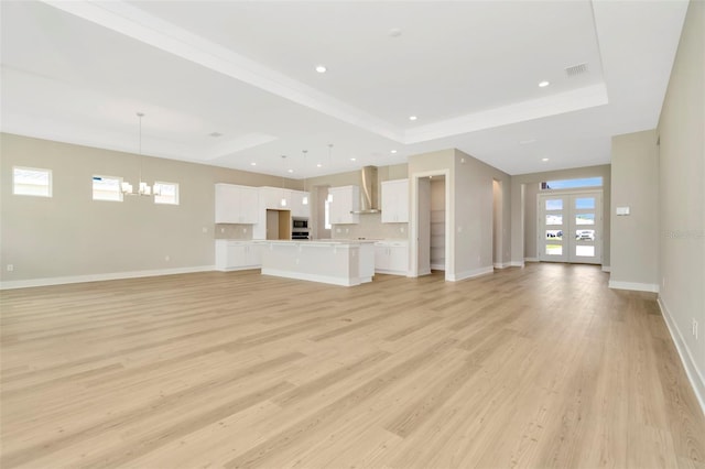 unfurnished living room featuring light wood-type flooring, a raised ceiling, french doors, and an inviting chandelier