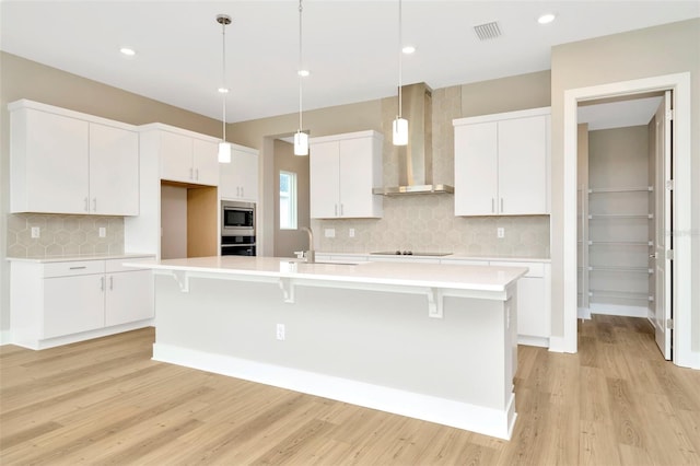 kitchen with wall chimney range hood, tasteful backsplash, white cabinets, and a kitchen island with sink