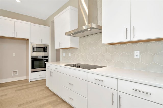 kitchen featuring wall chimney range hood, light hardwood / wood-style flooring, backsplash, white cabinets, and appliances with stainless steel finishes