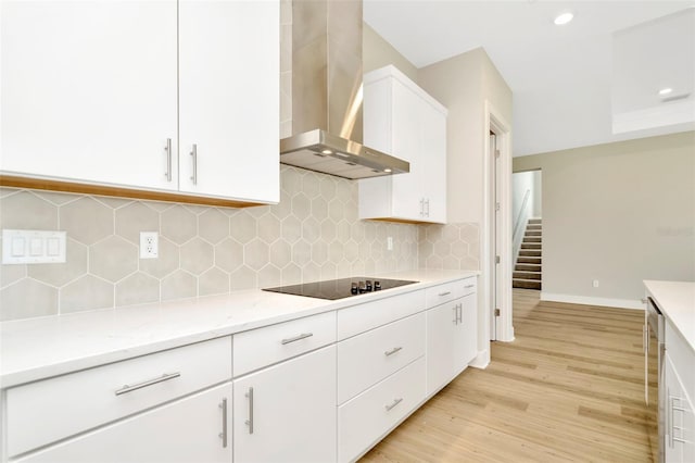 kitchen featuring black electric stovetop, light wood-type flooring, decorative backsplash, white cabinetry, and wall chimney range hood