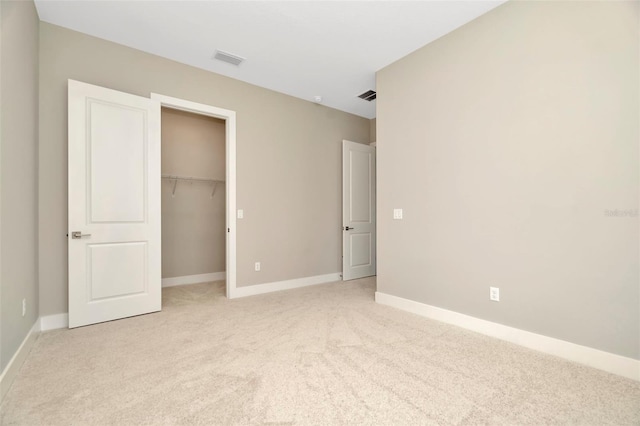 unfurnished bedroom featuring a walk in closet, a closet, and light carpet