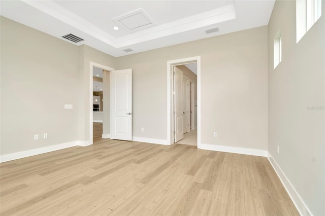 unfurnished bedroom with connected bathroom, a raised ceiling, and light wood-type flooring