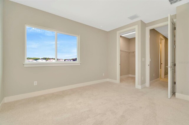 unfurnished bedroom featuring a spacious closet, a closet, and light carpet