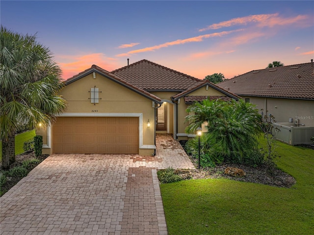 view of front of house with a yard, decorative driveway, an attached garage, and stucco siding