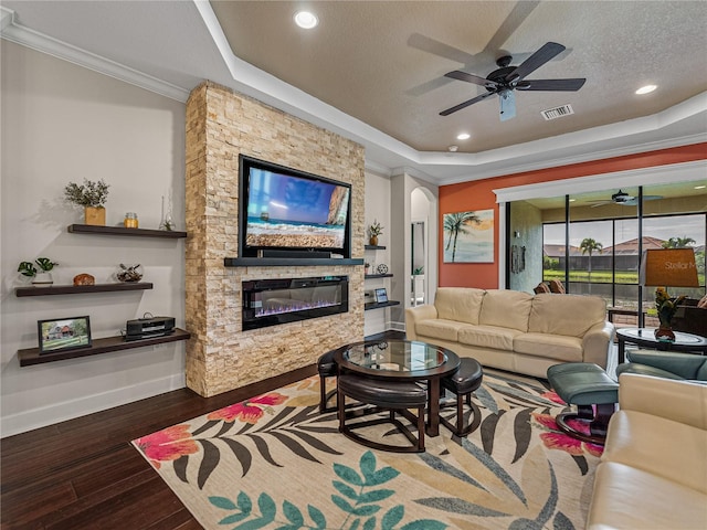 living room with a fireplace, a textured ceiling, wood-type flooring, ceiling fan, and a raised ceiling