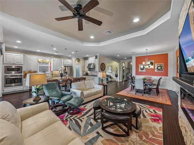 living room with a tray ceiling, ornamental molding, ceiling fan with notable chandelier, and dark hardwood / wood-style flooring