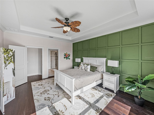 bedroom with a raised ceiling, ceiling fan, ensuite bathroom, and dark wood-type flooring