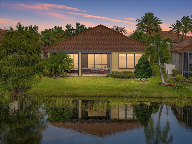 back house at dusk featuring a yard, a water view, and a patio area