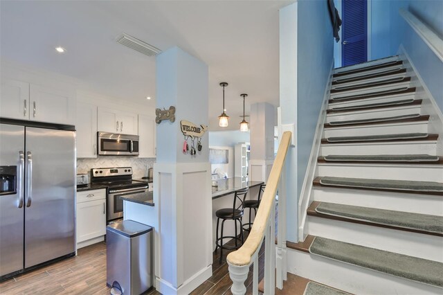 kitchen with a kitchen breakfast bar, wood-type flooring, tasteful backsplash, stainless steel appliances, and white cabinets