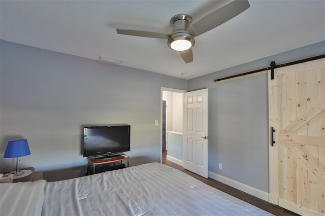 unfurnished bedroom with ceiling fan, hardwood / wood-style flooring, and a barn door