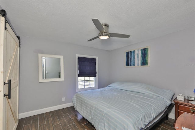 bedroom with ceiling fan, a barn door, a textured ceiling, and dark hardwood / wood-style flooring