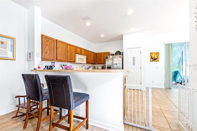 kitchen featuring a breakfast bar, kitchen peninsula, light hardwood / wood-style flooring, and stainless steel refrigerator with ice dispenser