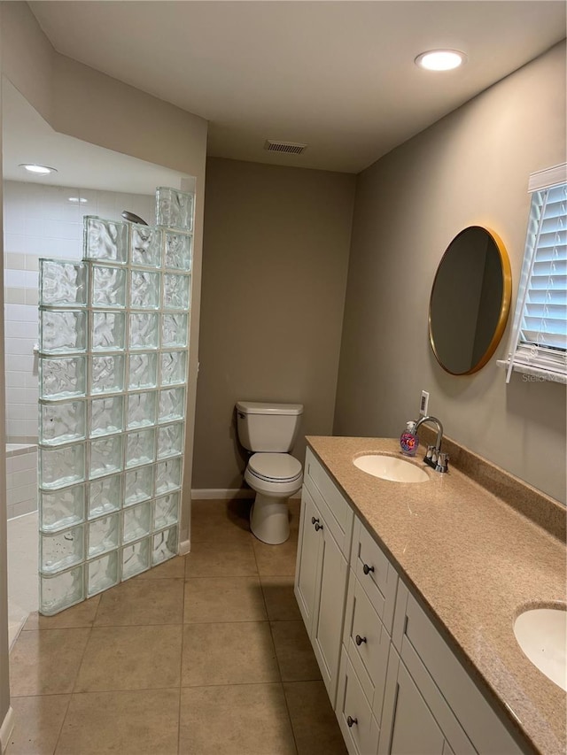 bathroom with toilet, vanity, tiled shower, and tile patterned floors