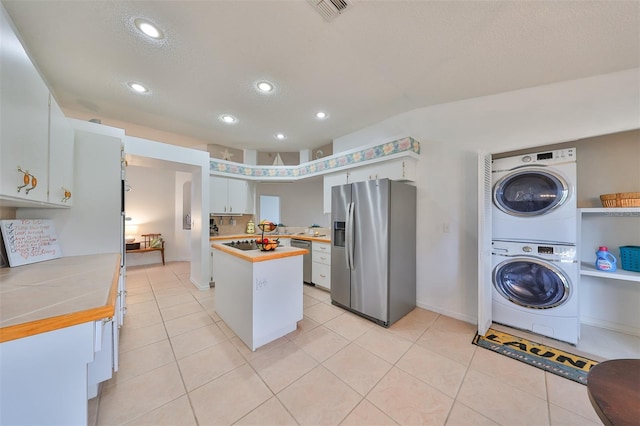 kitchen featuring white cabinets, a kitchen island, appliances with stainless steel finishes, stacked washer / drying machine, and tile counters