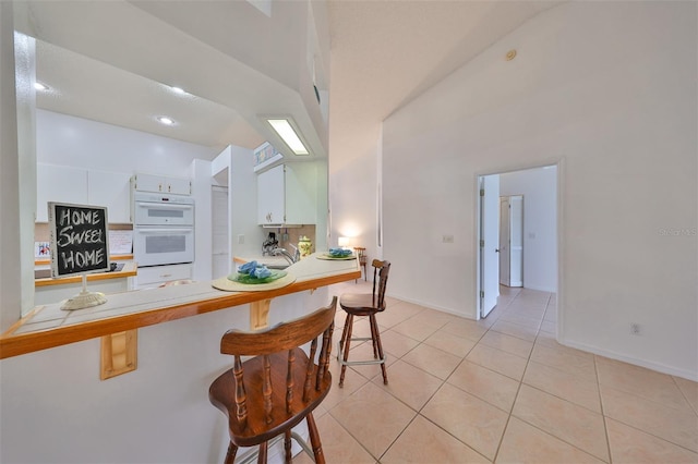 kitchen featuring double oven, kitchen peninsula, a kitchen breakfast bar, white cabinetry, and light tile patterned floors