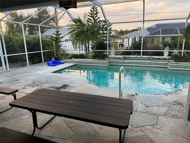 pool at dusk featuring glass enclosure and a patio area