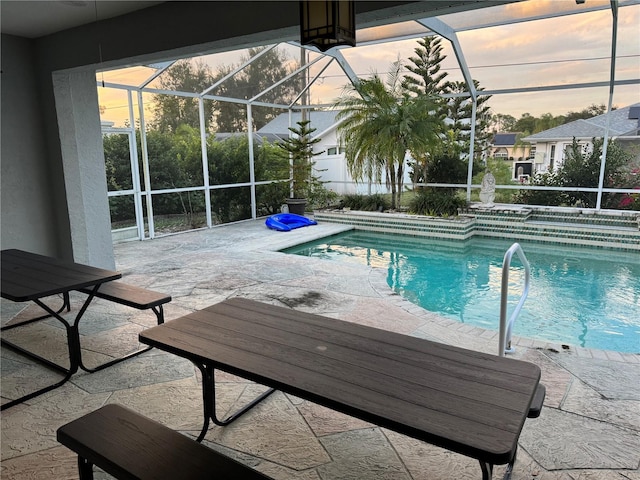 pool at dusk featuring glass enclosure and a patio area