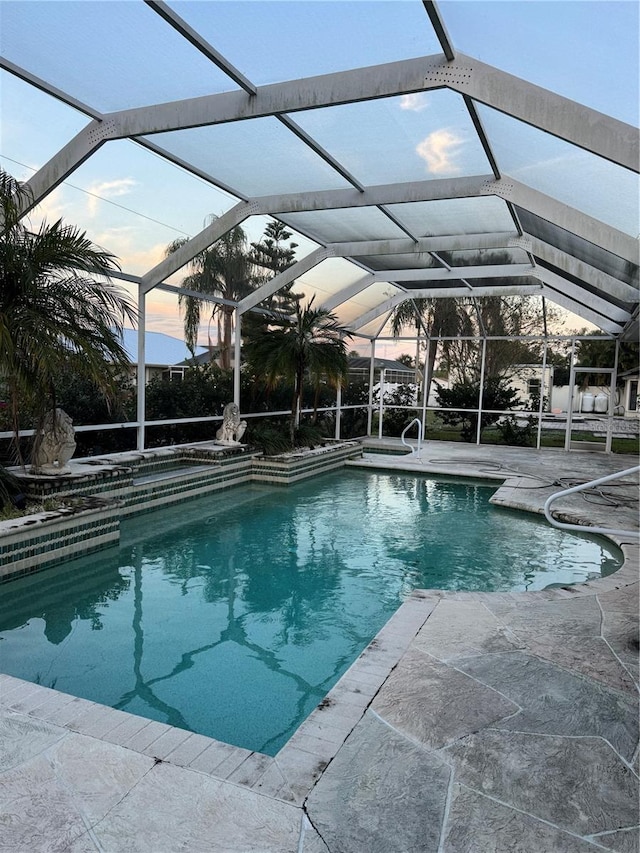 pool at dusk with glass enclosure and a patio