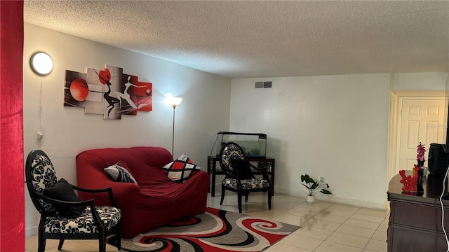 living area with a textured ceiling, light tile patterned flooring, visible vents, and baseboards