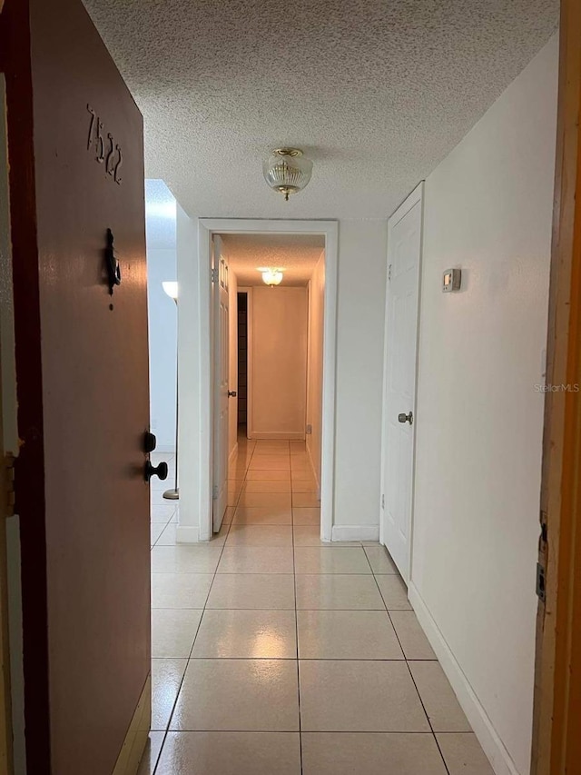 hallway featuring light tile patterned flooring, a textured ceiling, and baseboards