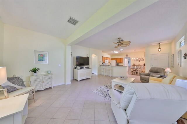 tiled living room with ceiling fan with notable chandelier