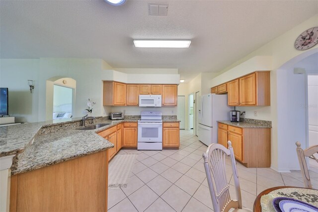 kitchen with sink, light stone counters, white appliances, light tile patterned floors, and kitchen peninsula