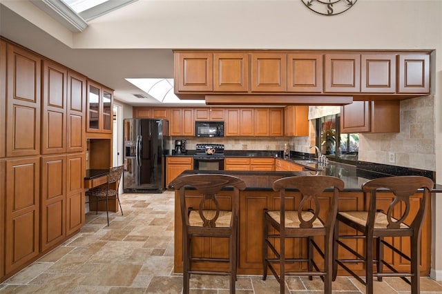 kitchen featuring a skylight, tasteful backsplash, kitchen peninsula, a breakfast bar, and black appliances