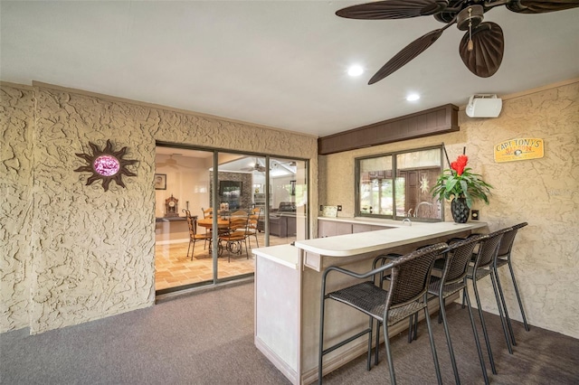 interior space with a breakfast bar, ceiling fan, kitchen peninsula, and crown molding