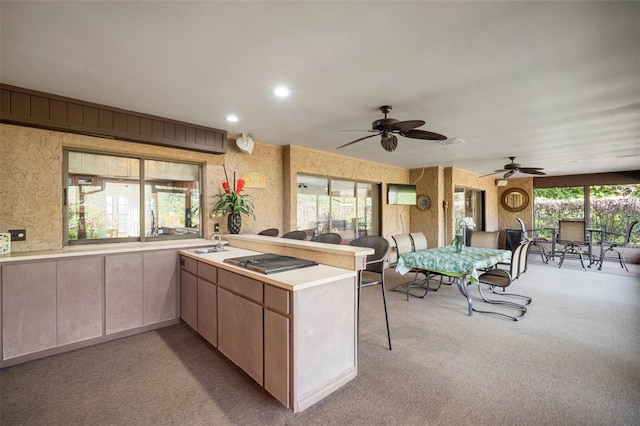 kitchen featuring ceiling fan, light colored carpet, kitchen peninsula, and sink