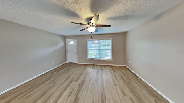 interior space with a textured ceiling, light wood-type flooring, a ceiling fan, and baseboards