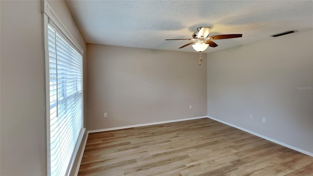 unfurnished room with a textured ceiling, light wood-style flooring, visible vents, baseboards, and a ceiling fan