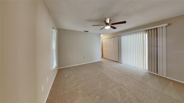 carpeted empty room featuring baseboards, ceiling fan, visible vents, and a textured ceiling