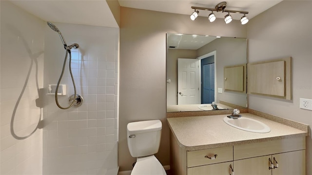 bathroom with toilet, tiled shower, and vanity