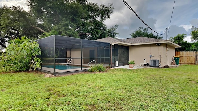 rear view of house featuring glass enclosure, central AC unit, a lawn, a fenced in pool, and stucco siding