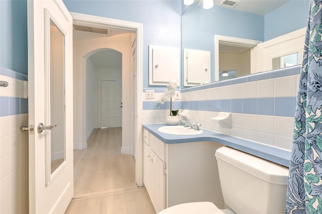 bathroom featuring decorative backsplash, toilet, vanity, wood-type flooring, and tile walls