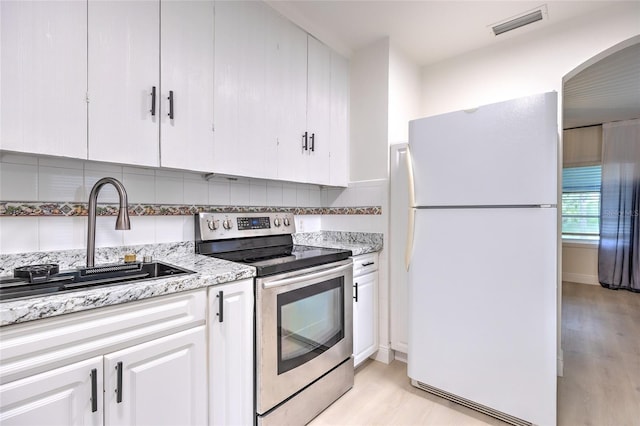 kitchen featuring light hardwood / wood-style flooring, stainless steel electric stove, tasteful backsplash, white cabinets, and white fridge