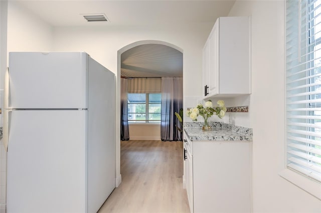 kitchen with light hardwood / wood-style floors, white refrigerator, light stone countertops, and white cabinetry