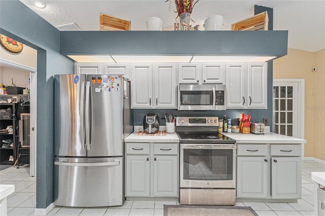 kitchen featuring stainless steel appliances, light tile patterned flooring, and vaulted ceiling