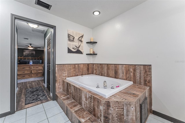 bathroom with tile patterned flooring, tiled bath, ceiling fan, and a textured ceiling