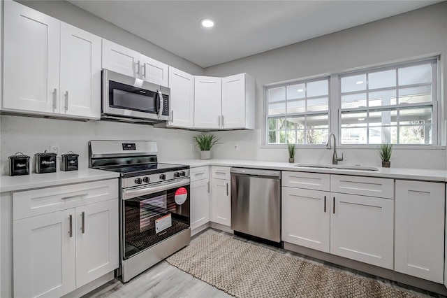 kitchen featuring appliances with stainless steel finishes, white cabinetry, light wood-type flooring, and sink