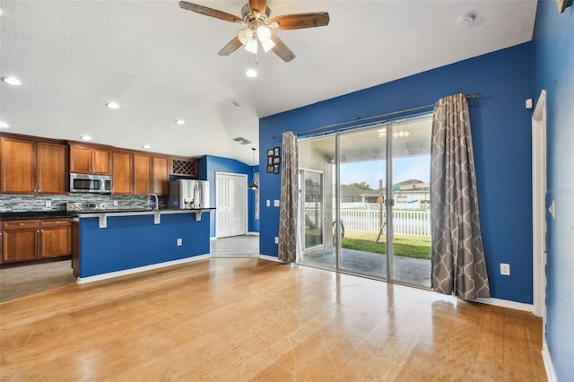 kitchen with stainless steel appliances, a kitchen bar, tasteful backsplash, a textured ceiling, and ceiling fan