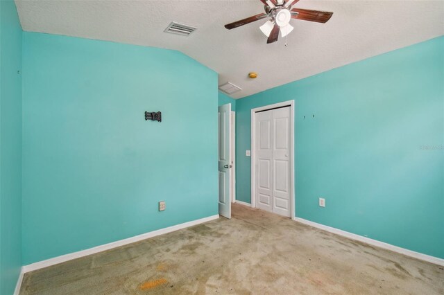 unfurnished bedroom with ceiling fan, vaulted ceiling, a textured ceiling, and light colored carpet