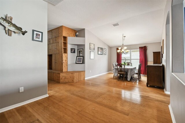 unfurnished dining area featuring a textured ceiling, lofted ceiling, an inviting chandelier, and wood-type flooring