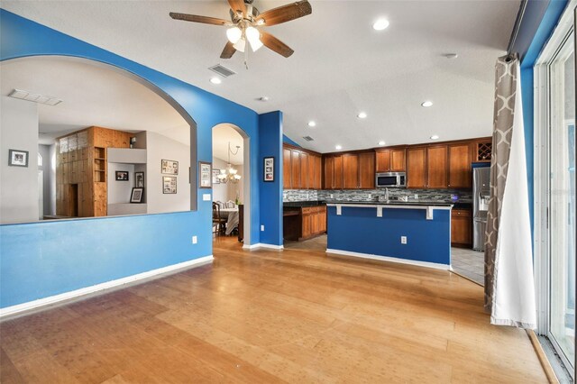 kitchen featuring appliances with stainless steel finishes, decorative backsplash, light wood-type flooring, ceiling fan with notable chandelier, and a center island