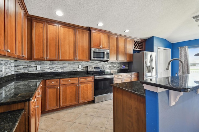 6843 Runner Oak Dr, Wesley Chapel, FL 33545 - kitchen featuring light tile patterned floors, stainless steel appliances, dark stone countertops, and brown cabinets