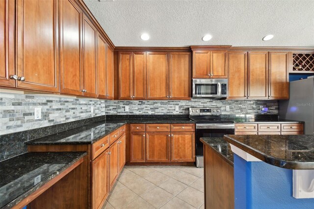 kitchen with stainless steel appliances, tasteful backsplash, a textured ceiling, light tile patterned floors, and dark stone countertops