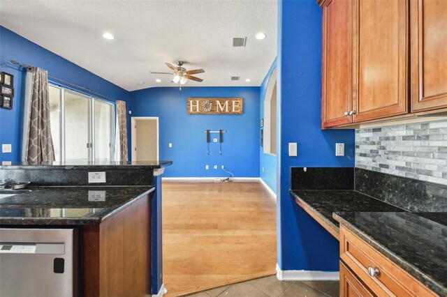 kitchen with ceiling fan, decorative backsplash, dishwashing machine, light tile patterned floors, and dark stone countertops